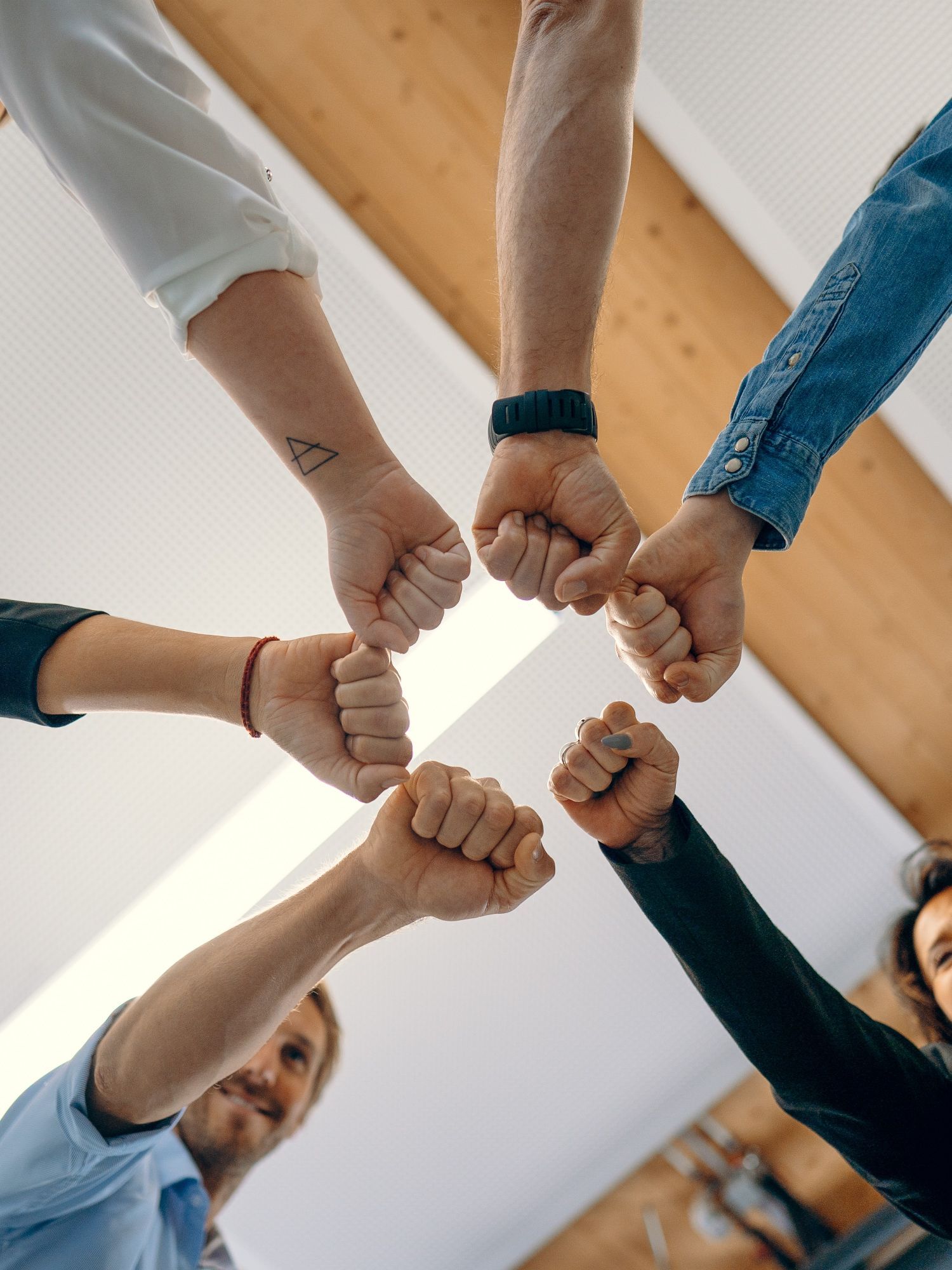 Ein Foto, dass Team-Spirit repräsentieren soll. MitarbeiterInnen stehen im Kreis und halten die Faust aneinander
